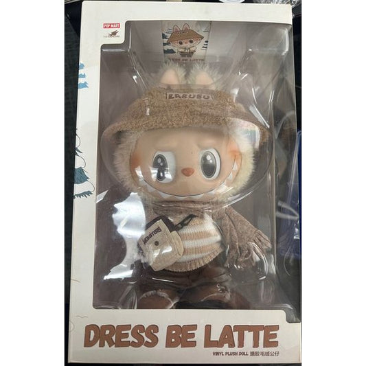 The Dress Be Latte doll from Pop Mart's The Monsters series showcases Labubu, the mischievous yet endearing character, in a cozy, winter-ready ensemble. Dressed in a plush bunny-eared hat, a knitted scarf, a fuzzy sweater, and snow boots, Labubu exudes charm and warmth. The doll's face and ears feature soft, fur-like materials, adding a tactile element to its design. Standing at approximately 15 inches tall, it combines vinyl durability with plush comfort, making it a standout piece for collectors and fans